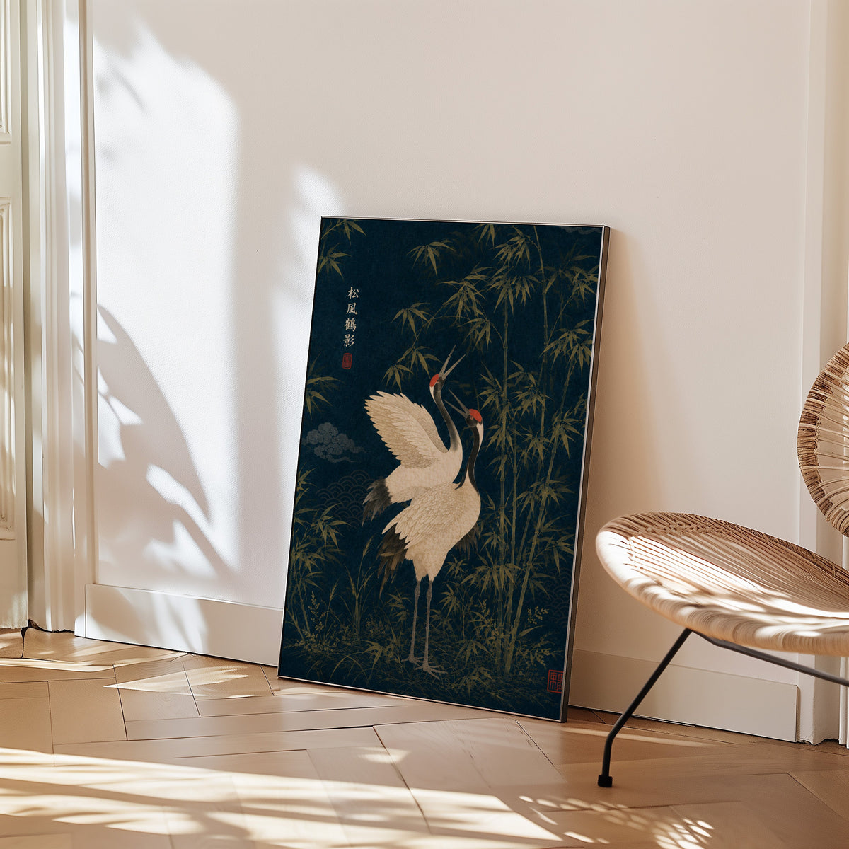 red-crowned cranes and bamboo on navy print in a black frame leaning on a herringbone floor beside a woven rattan chair