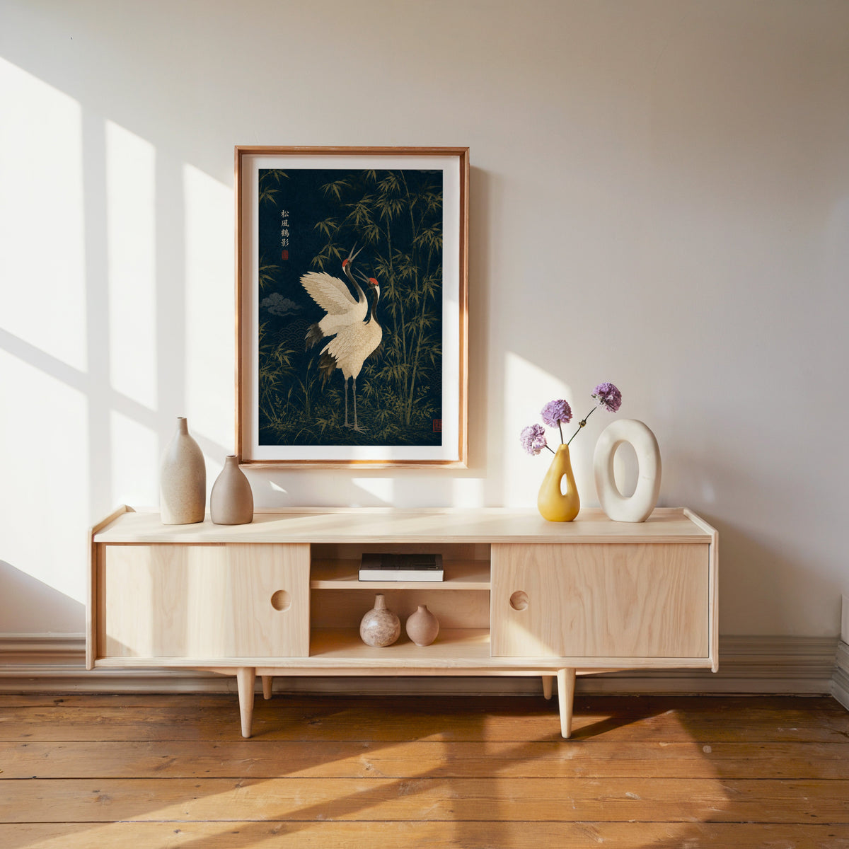 red-crowned cranes and bamboo on navy print shown in a wood frame with a white mat above a pale wood media console
