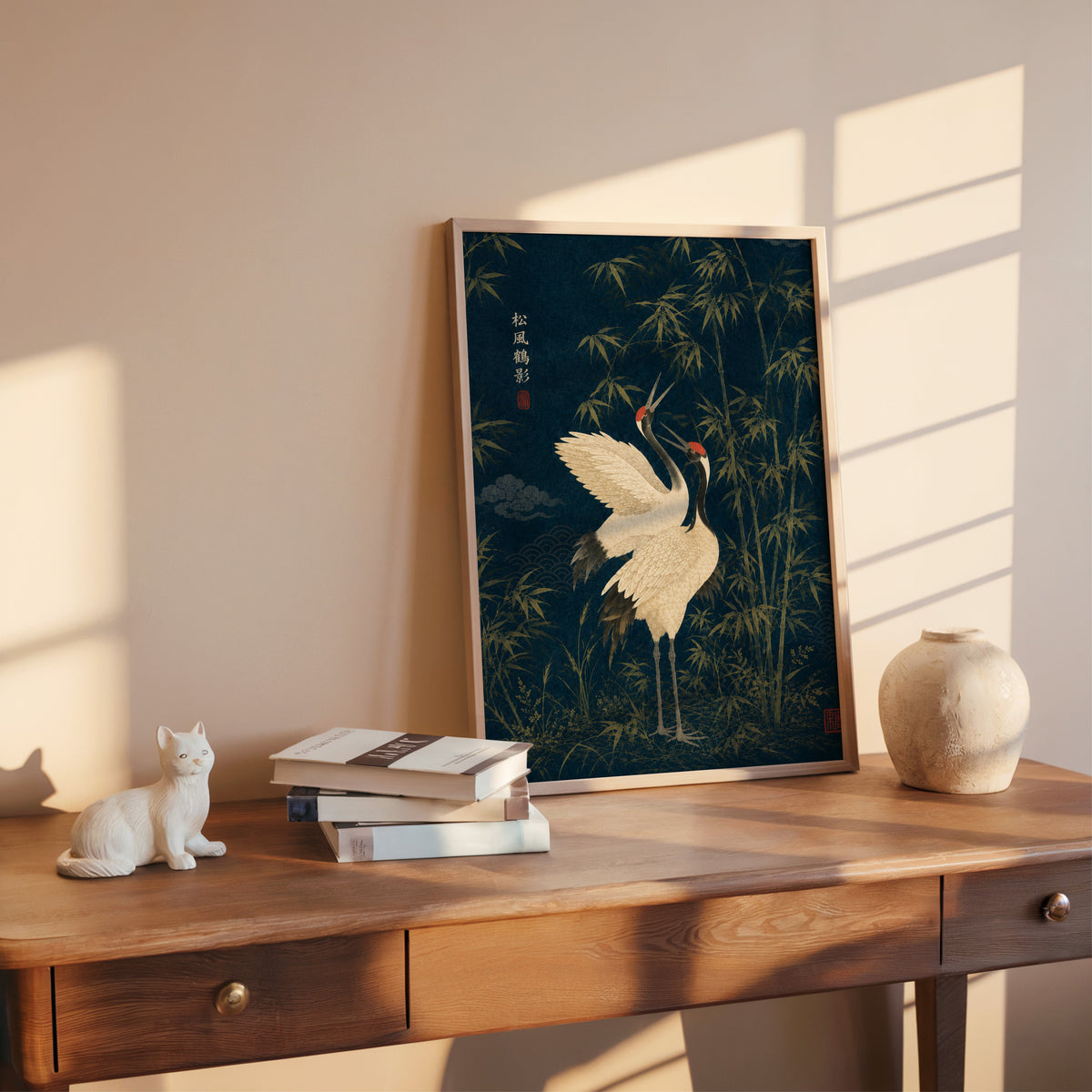 red-crowned cranes and bamboo on navy print shown in a rose gold frame leaning on a wooden writing desk with books