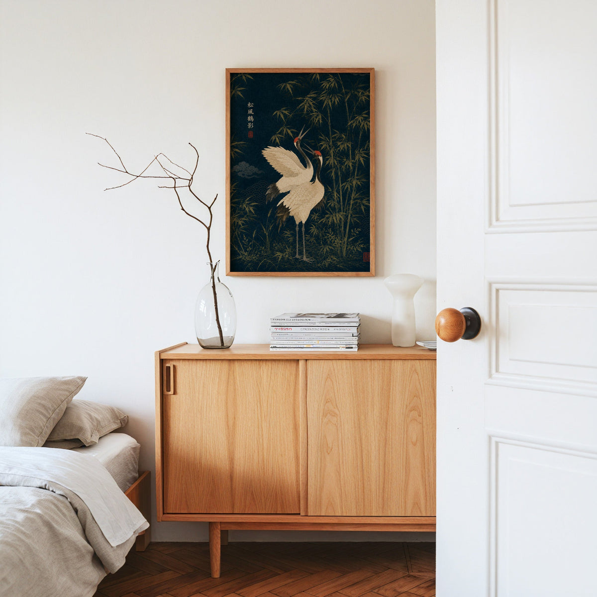 red-crowned cranes and bamboo on navy print in an oak frame above an oak sideboard in a bedroom with linen bedding