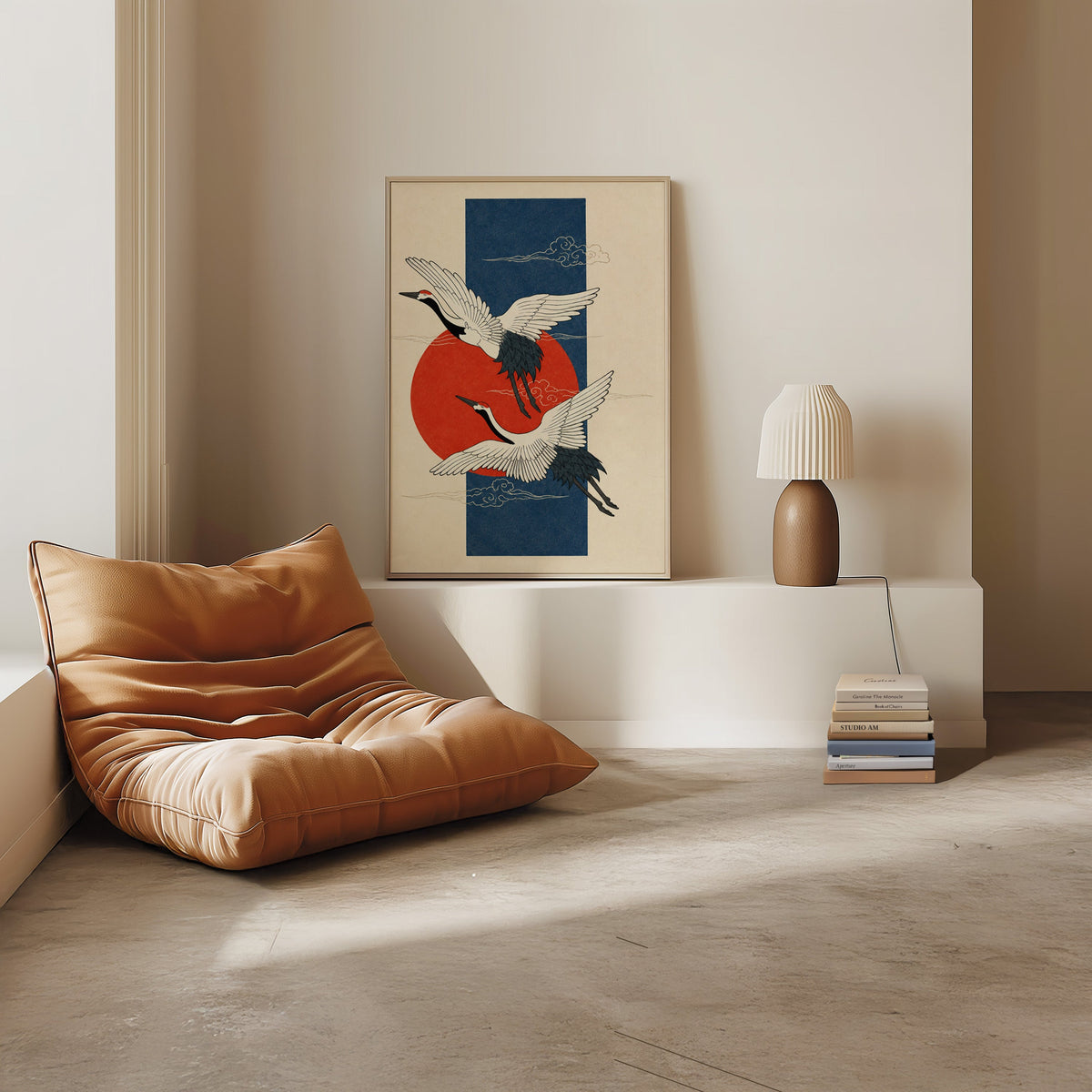 red-crowned cranes on navy with red sun print in a light oak frame on a white ledge by a tan leather floor chair