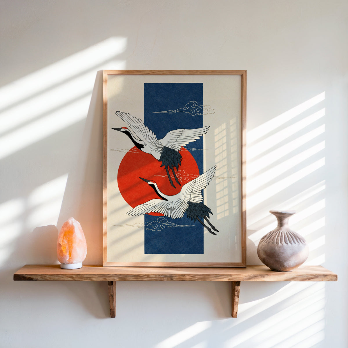 red-crowned cranes on navy with red sun print in an oak frame on a live-edge wall shelf with a salt lamp and clay vase
