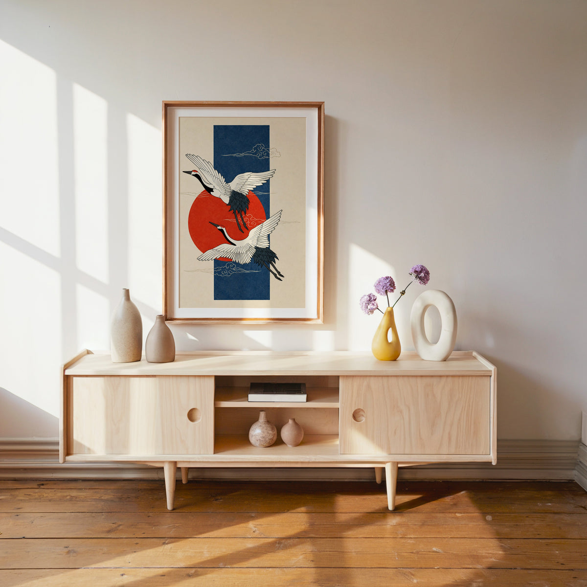 red-crowned cranes on navy with red sun print shown in a wood frame with a white mat above a pale wood media console