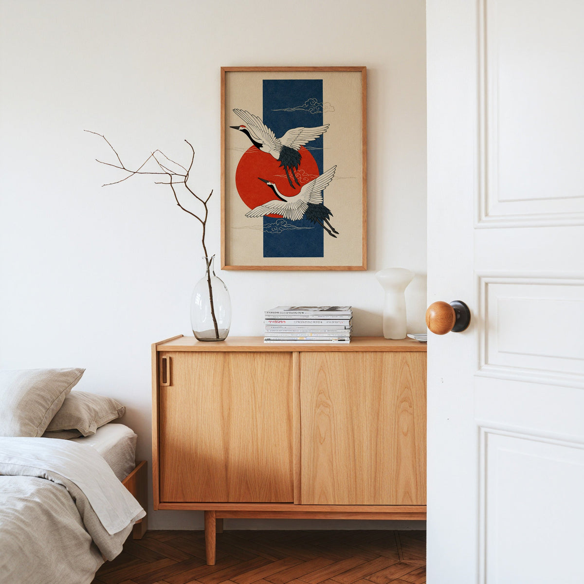 red-crowned cranes on navy with red sun print in an oak frame above an oak sideboard in a bedroom with linen bedding