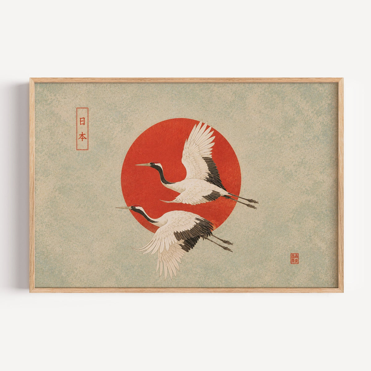 Red-crowned cranes flying past a red sun print in a light oak frame on a plain white wall
