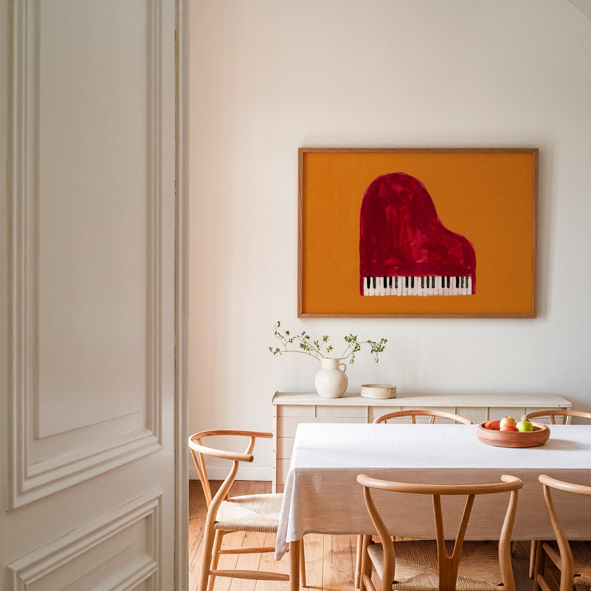 Orange and red piano print in an oak frame in a dining room with wishbone chairs