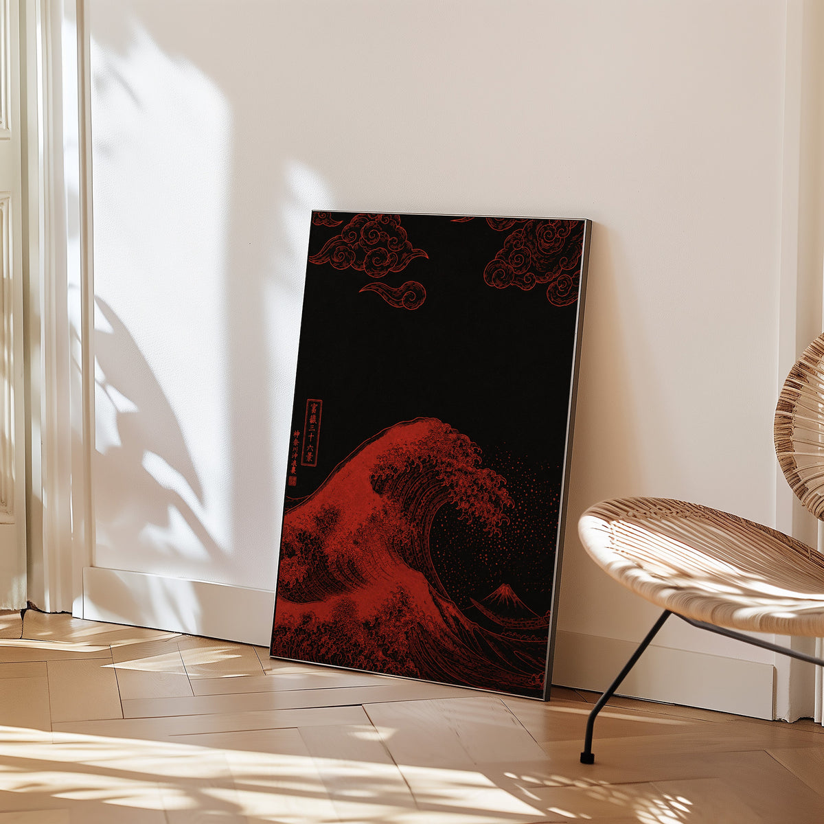 red Great Wave on black print in a black frame leaning on a herringbone floor beside a woven rattan chair