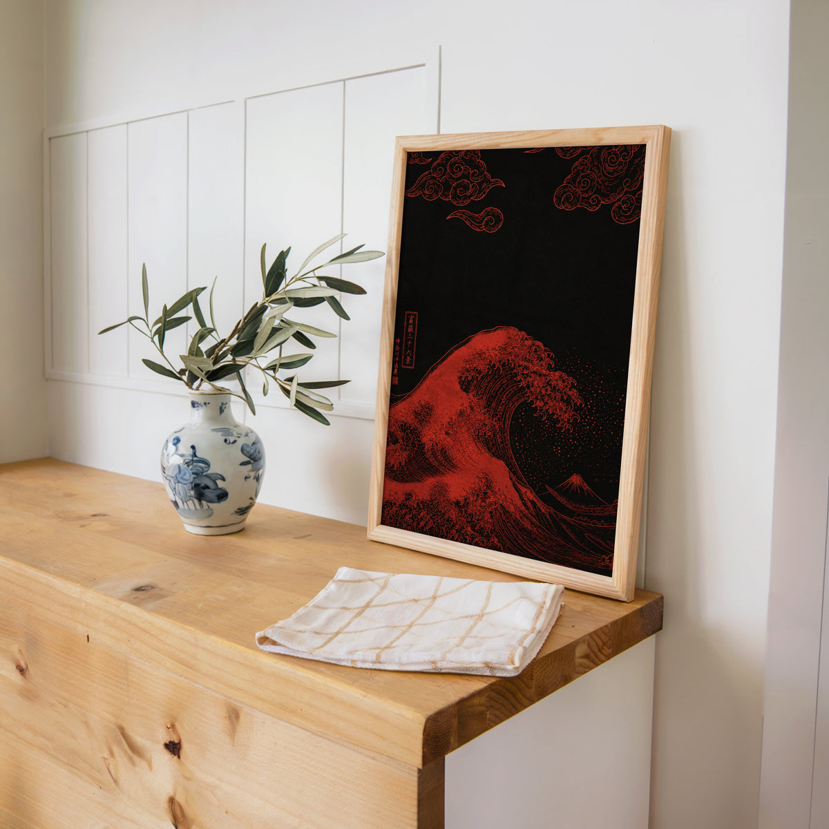 red Great Wave on black print in a pine frame on a wooden counter beside a blue and white porcelain vase