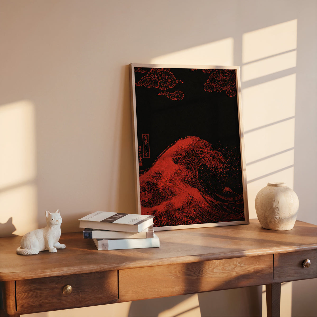 red Great Wave on black print shown in a rose gold frame leaning on a wooden writing desk with books