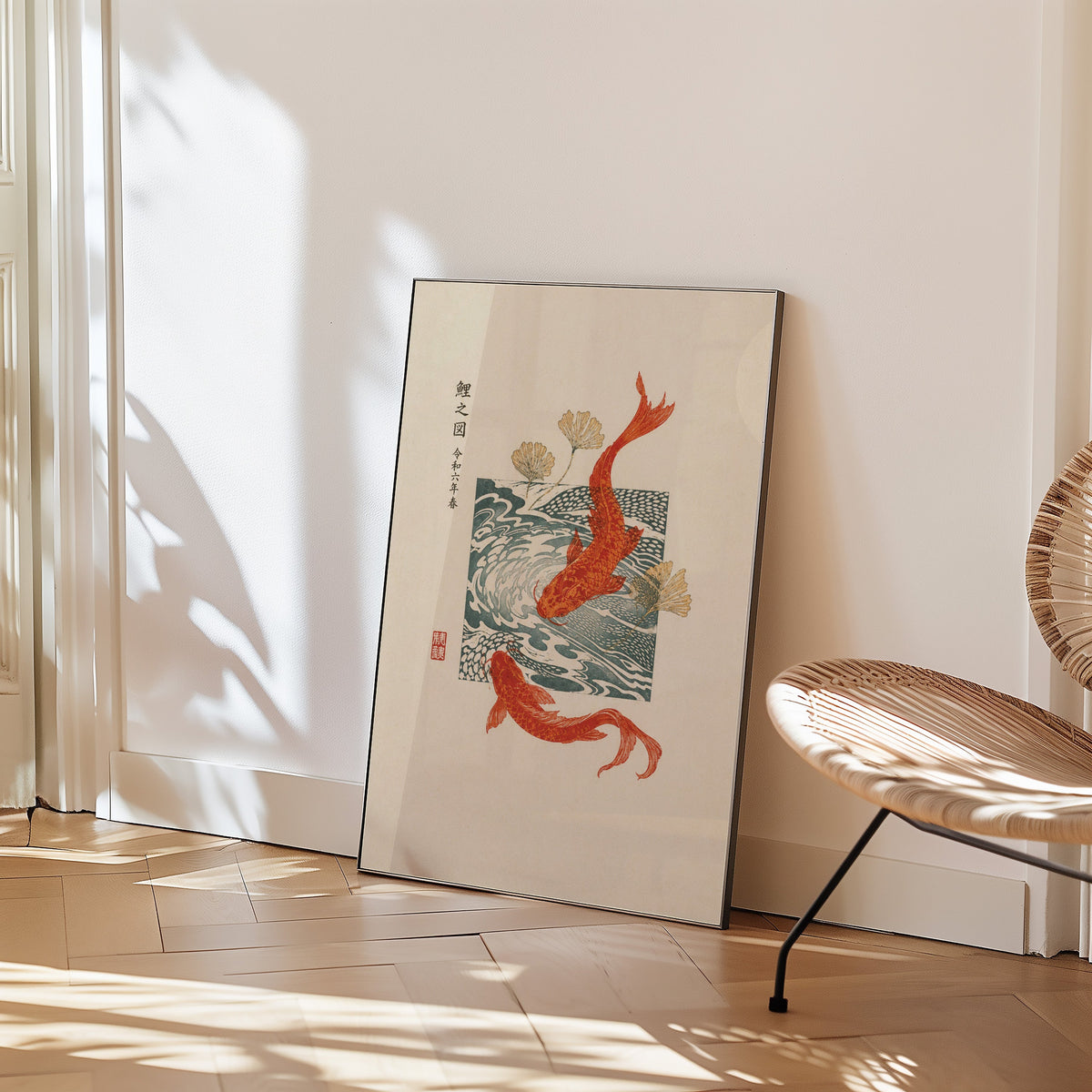 red koi with ginkgo and wave block print in a black frame leaning on a herringbone floor beside a woven rattan chair