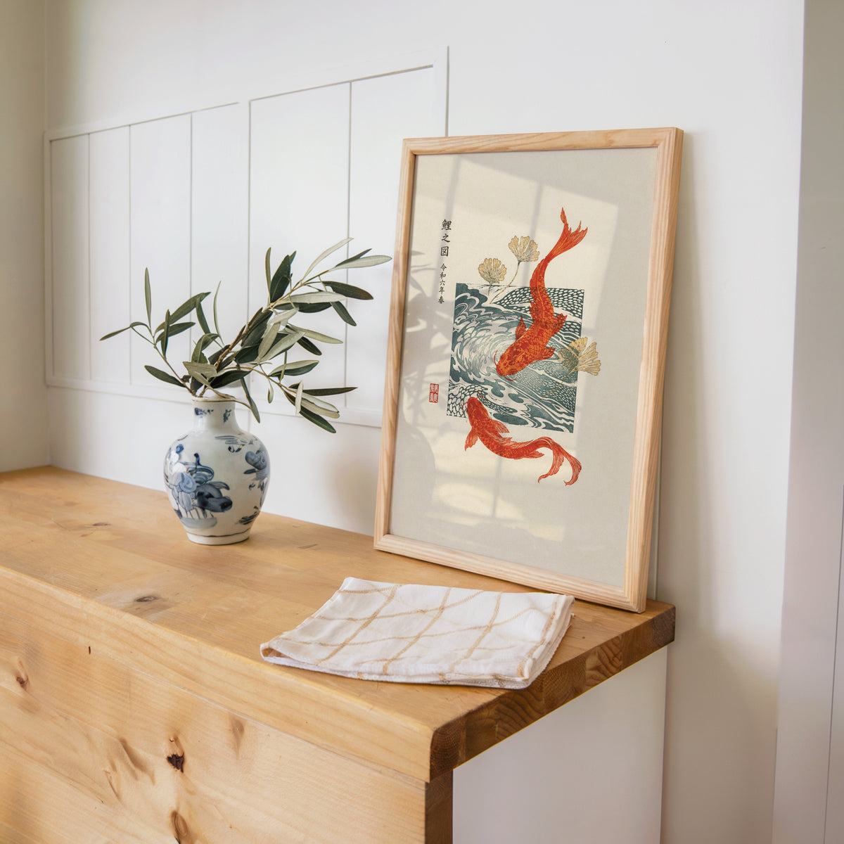 red koi with ginkgo and wave block print in a pine frame on a wooden counter beside a blue and white porcelain vase