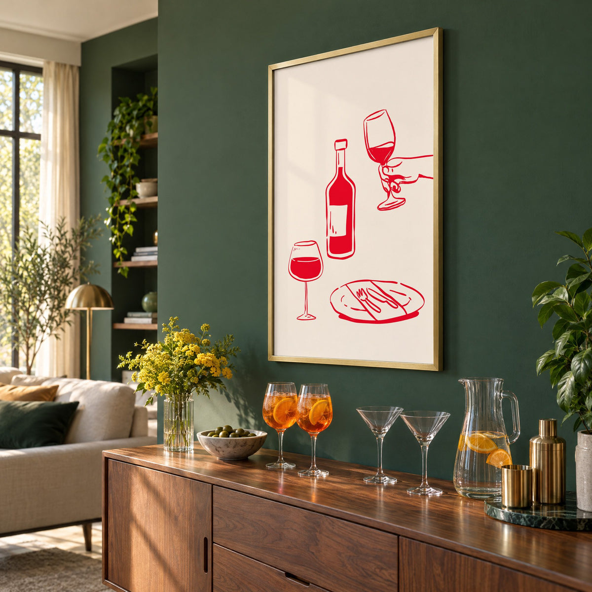 Red line wine bottle and dinner table print in a brass frame on a bottle green wall above a sideboard with spritz and martini glasses, seen at an angle