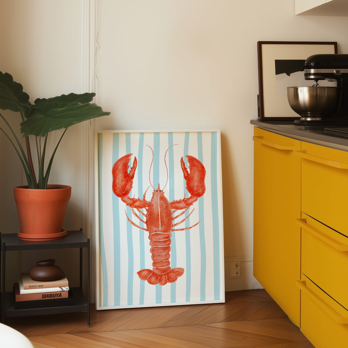 Red lobster print in a white frame leaning on parquet beside a bright yellow kitchen