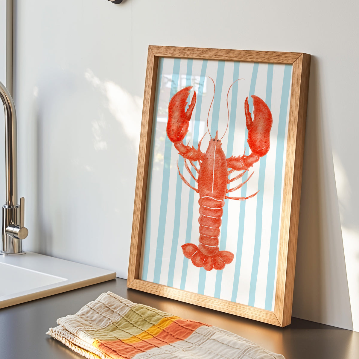 Red lobster print in an oak frame by the kitchen sink beside a striped tea towel