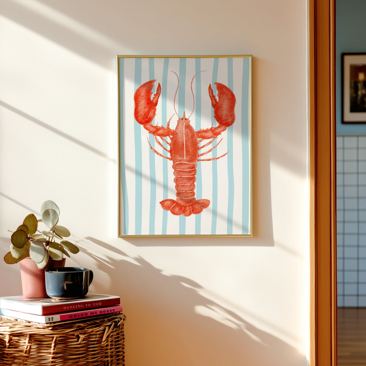Red lobster print shown in a gold frame above a basket of books and a pilea plant