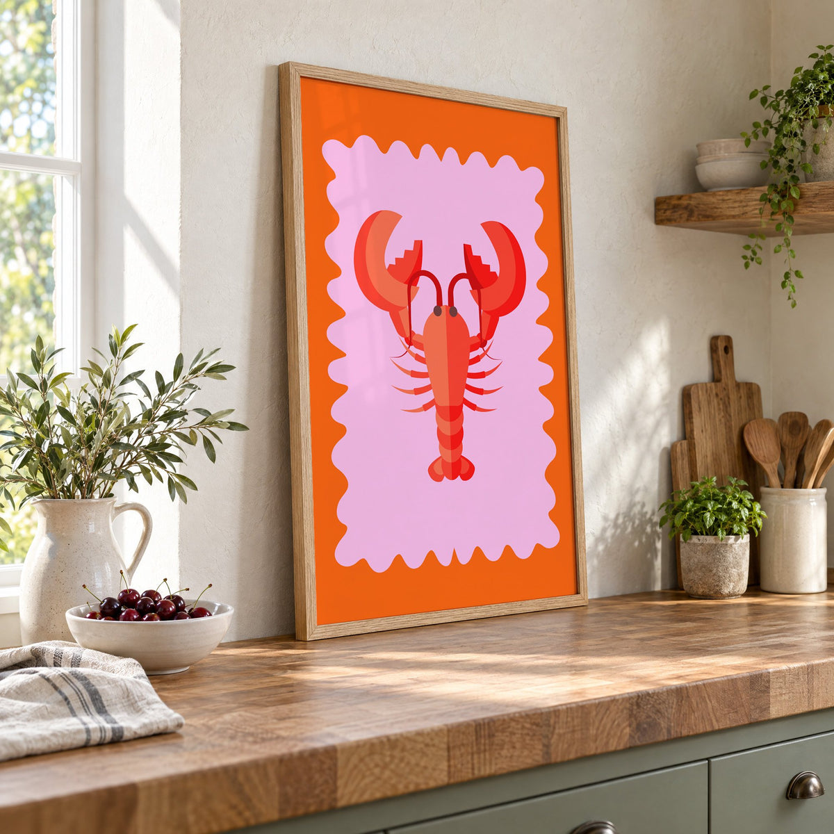 Red lobster pink wavy frame print in an oak frame leaning on a butcher block island beside a bowl of cherries