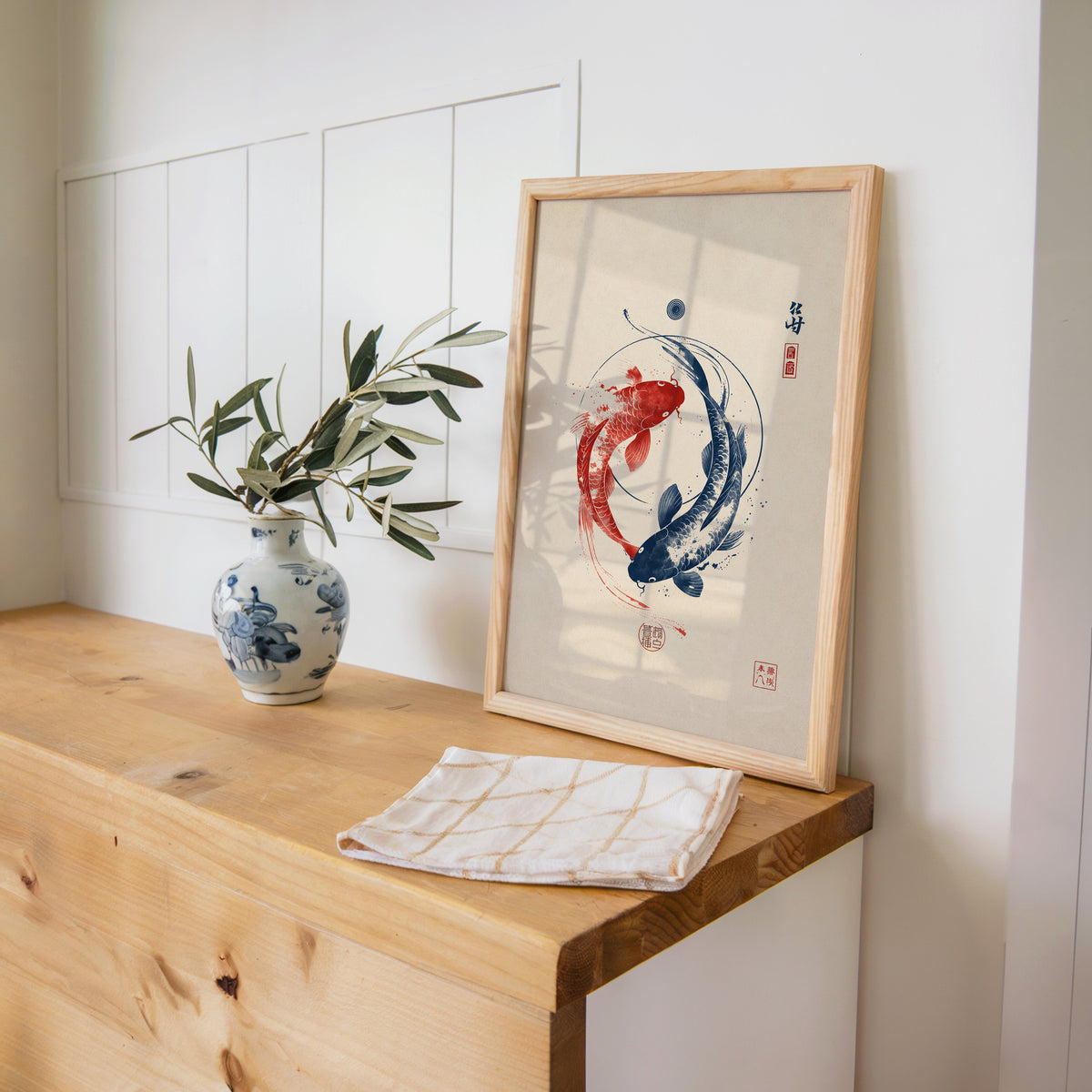 red and navy koi in a circle print in a pine frame on a wooden counter beside a blue and white porcelain vase