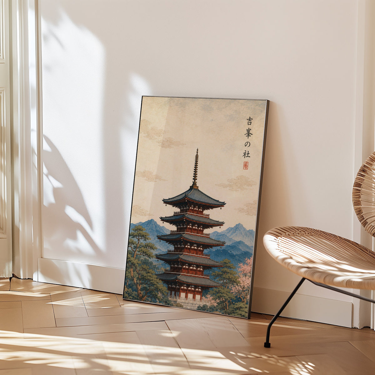 red pagoda with blue mountains print in a black frame leaning on a herringbone floor beside a woven rattan chair