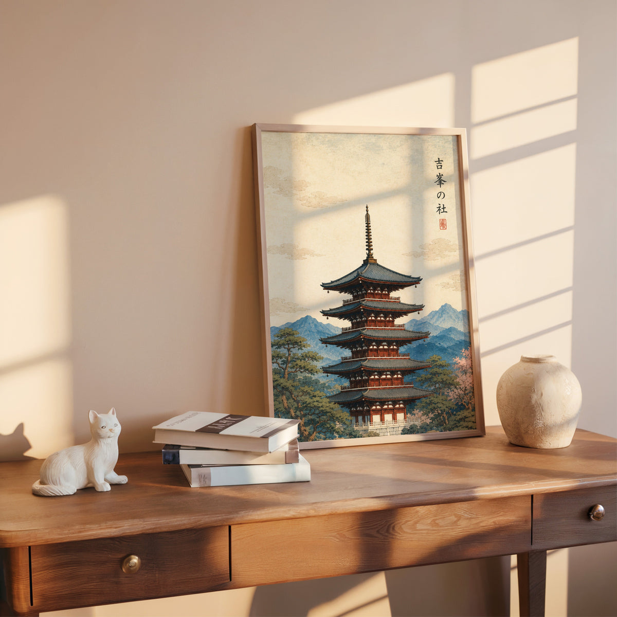 red pagoda with blue mountains print shown in a rose gold frame leaning on a wooden writing desk with books