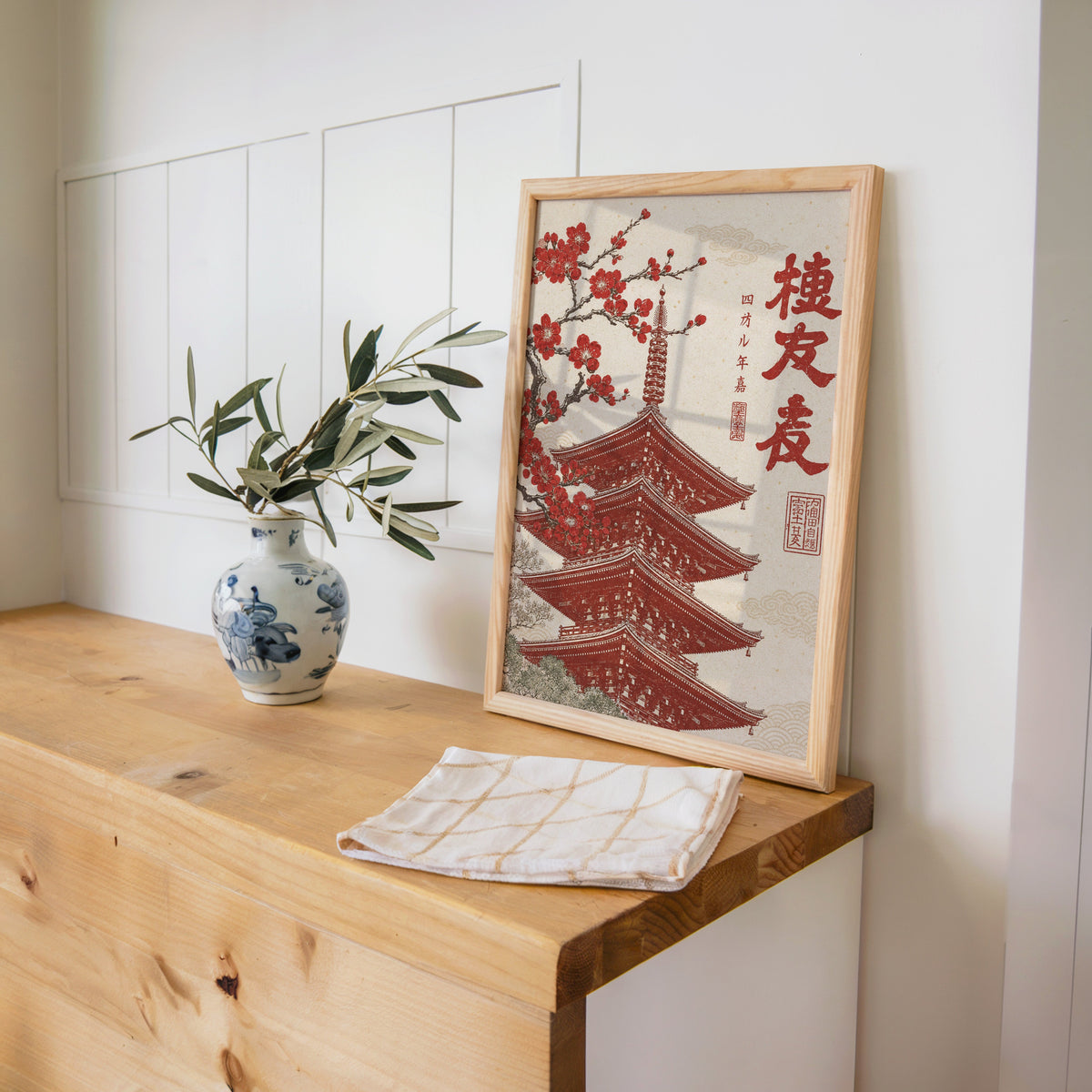 red engraved pagoda with blossom branch print in a pine frame on a wooden counter beside a blue and white porcelain vase