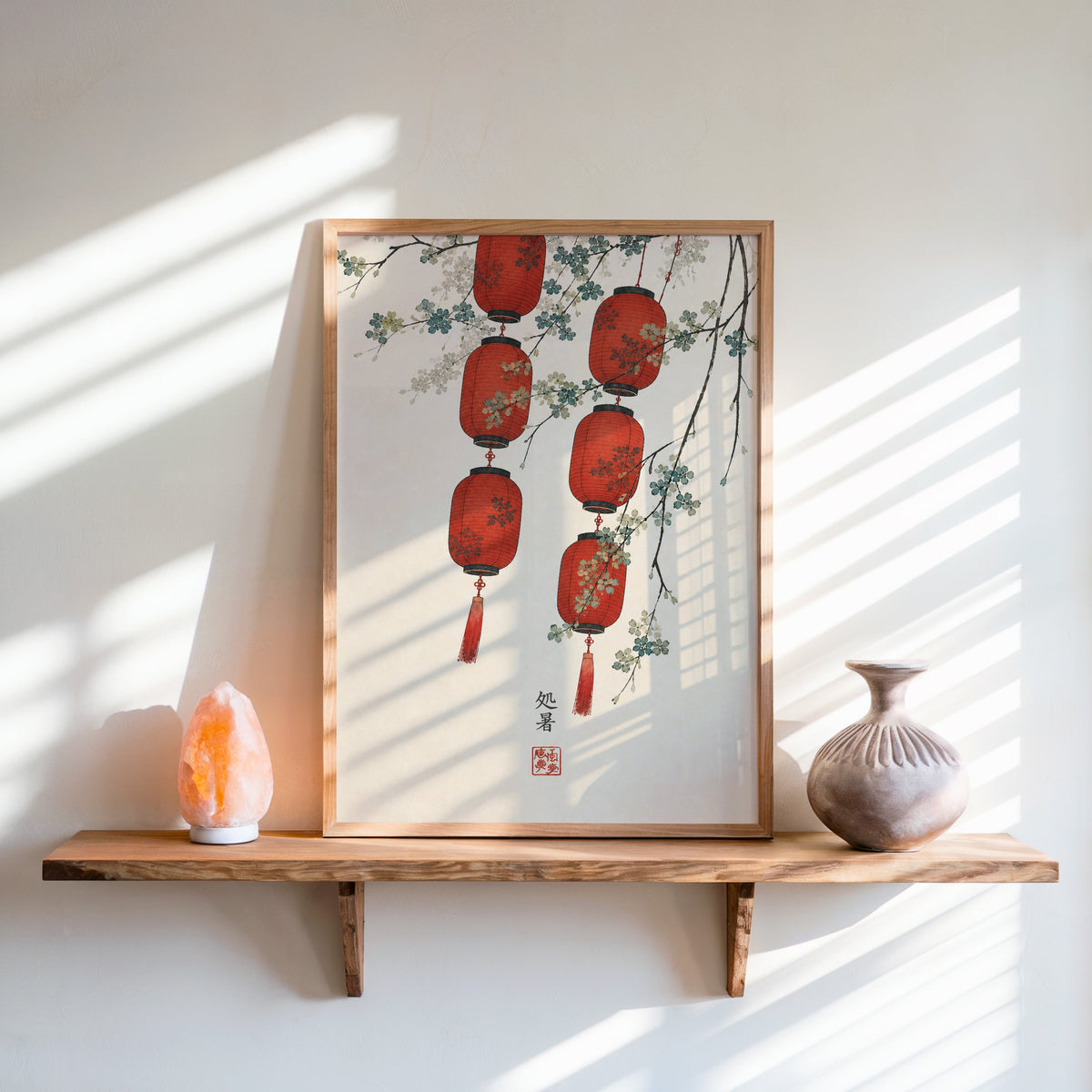 red paper lanterns with blossom branch print in an oak frame on a live-edge wall shelf with a salt lamp and clay vase
