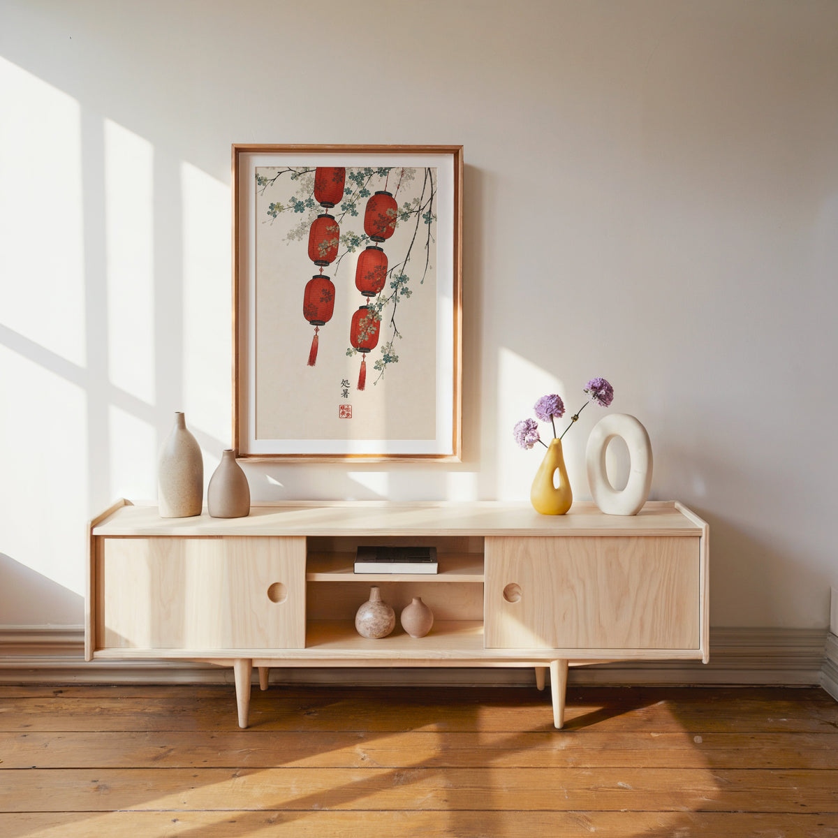 red paper lanterns with blossom branch print shown in a wood frame with a white mat above a pale wood media console