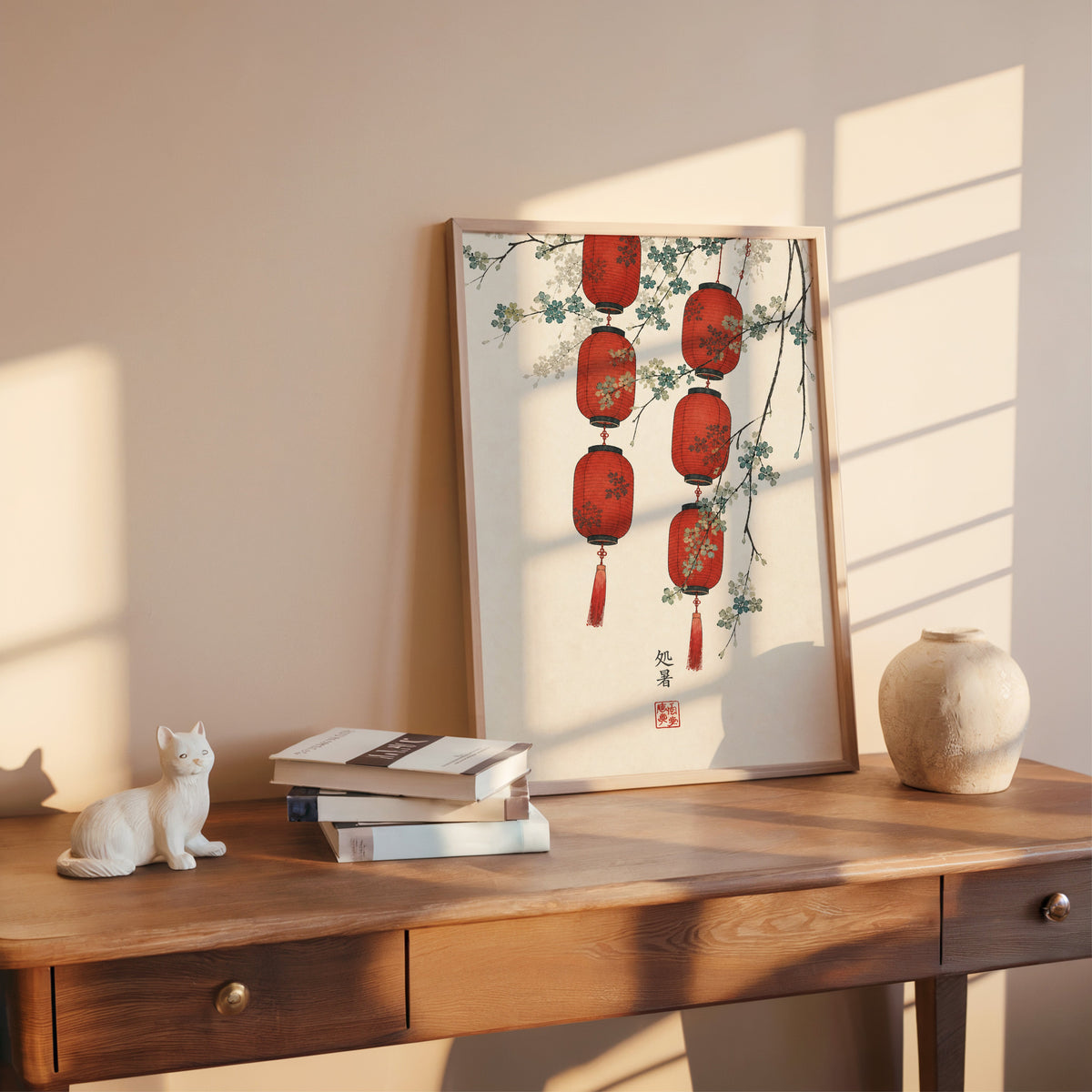 red paper lanterns with blossom branch print shown in a rose gold frame leaning on a wooden writing desk with books