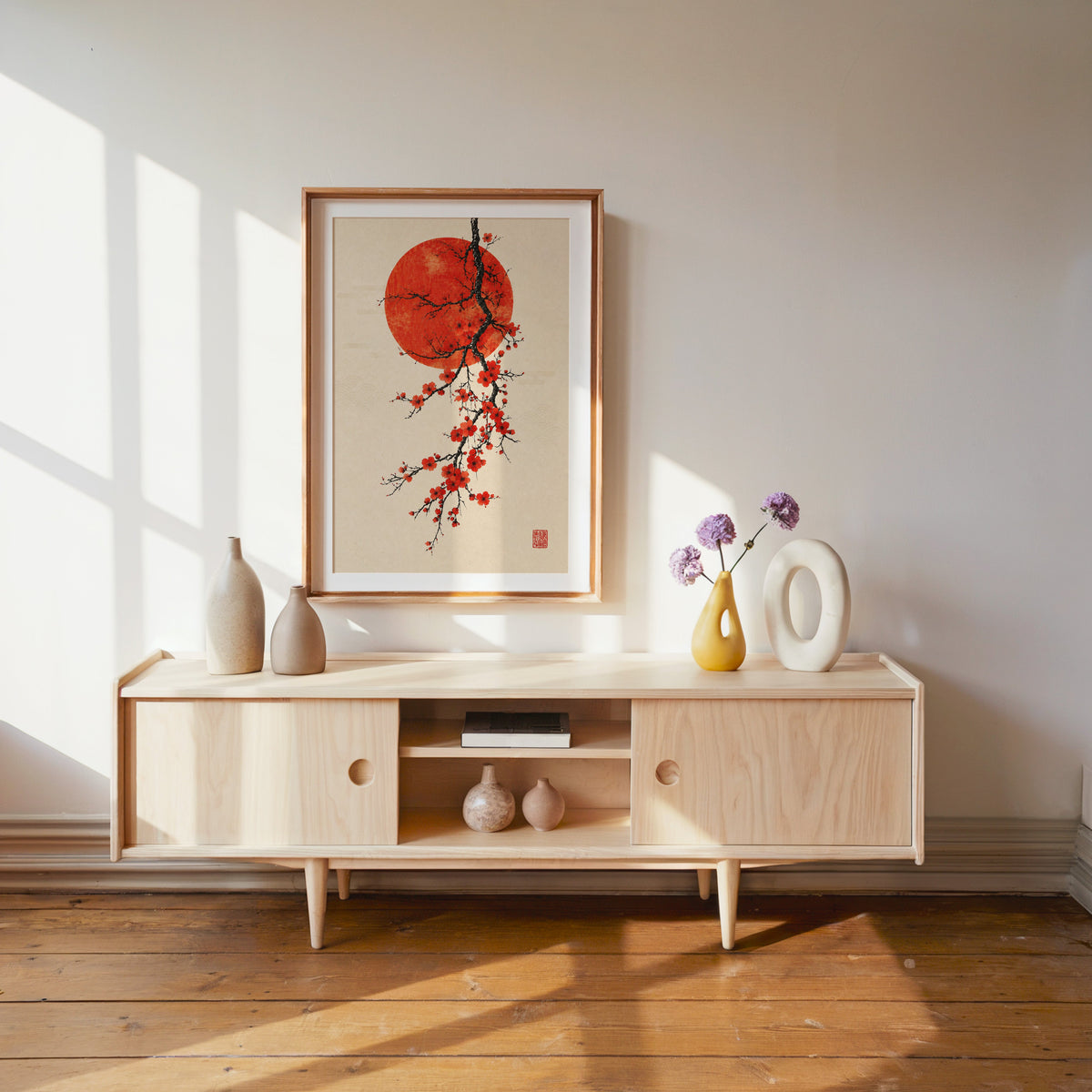 red blossom ink branch with red sun print shown in a wood frame with a white mat above a pale wood media console