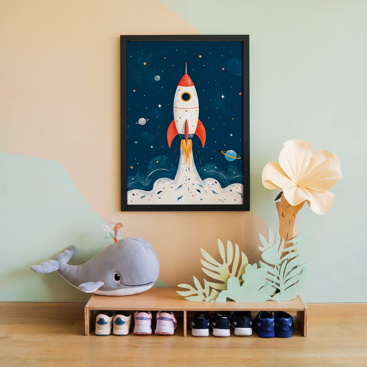 Red rocket launching past planets nursery print in a black frame on a mint and peach wall above a whale plush