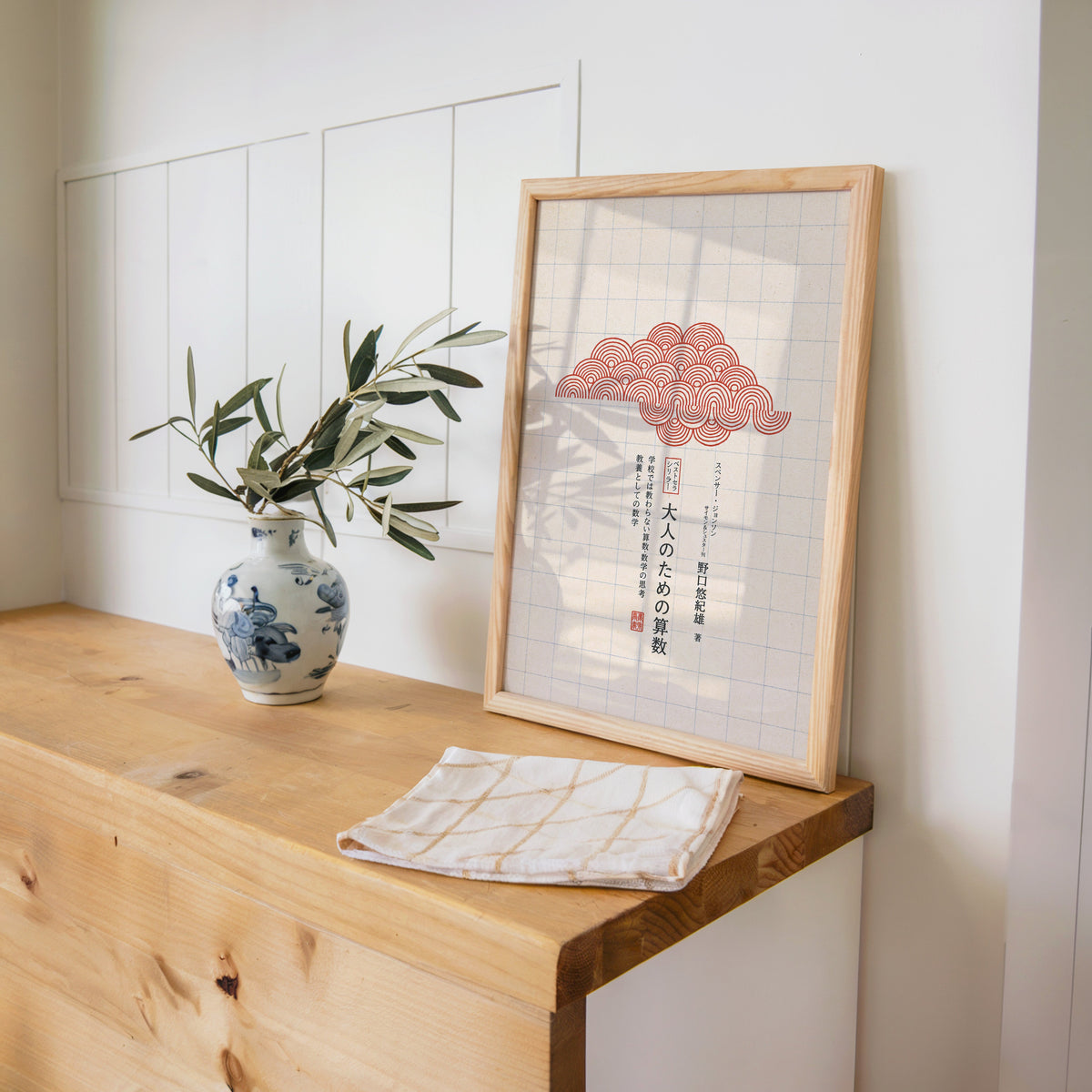 red seigaiha cloud on grid paper print in a pine frame on a wooden counter beside a blue and white porcelain vase