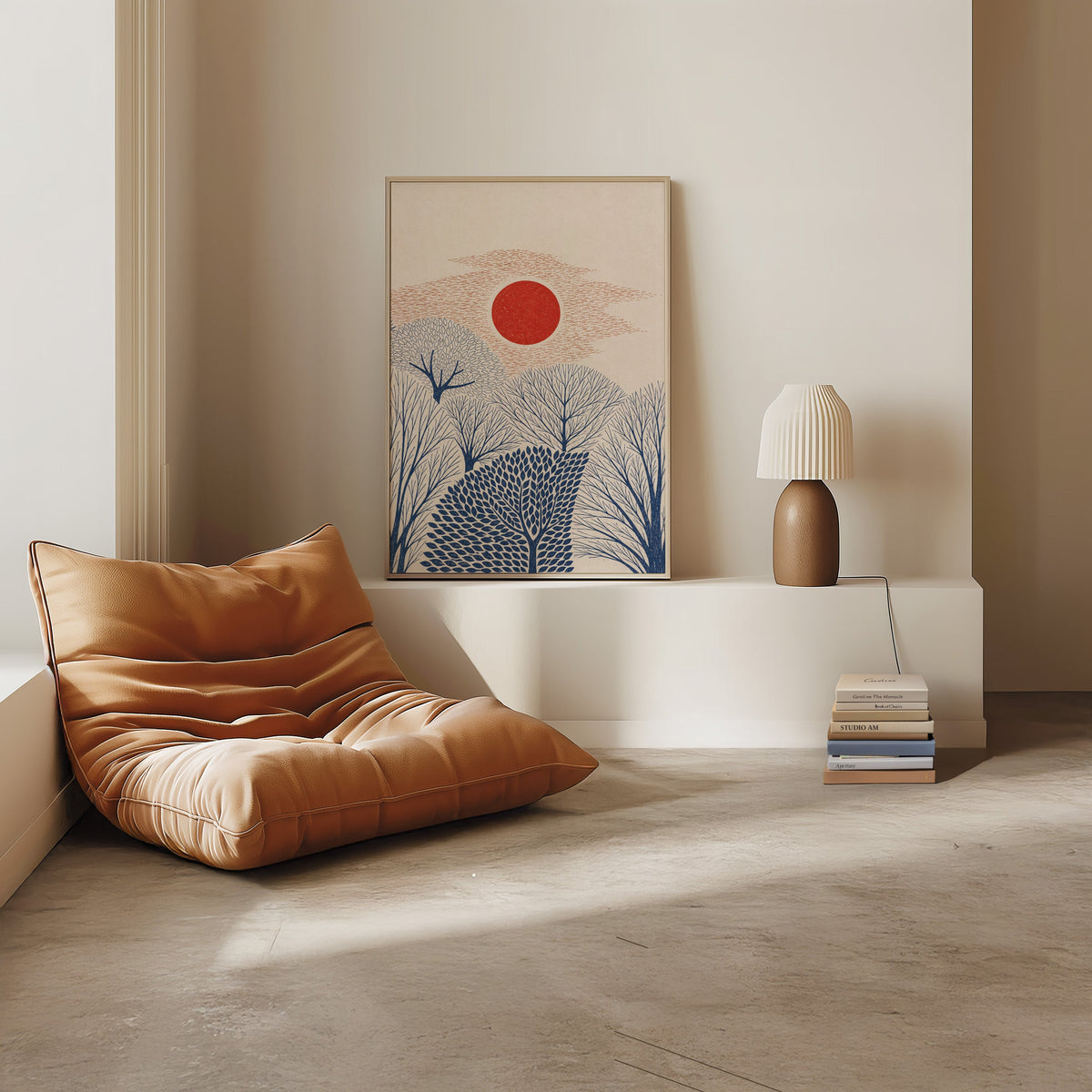 red sun over navy trees print in a light oak frame on a white ledge by a tan leather floor chair