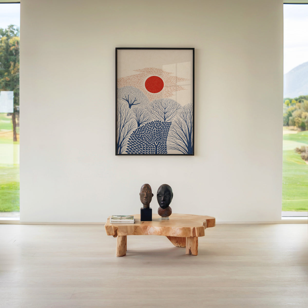 red sun over navy trees print in a black frame above a live-edge wood coffee table between garden windows