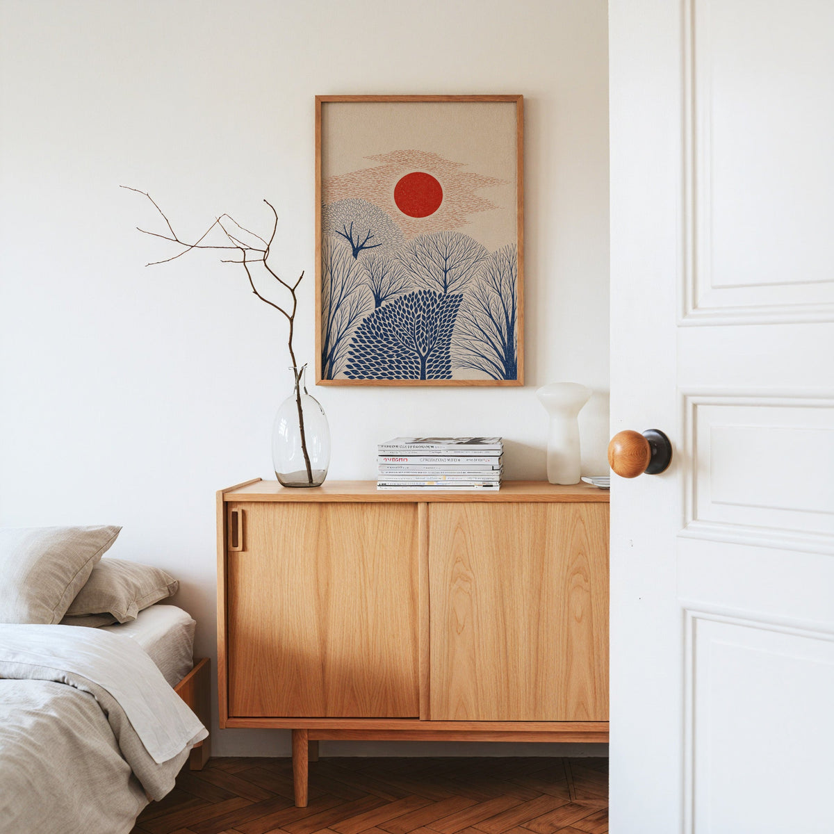 red sun over navy trees print in an oak frame above an oak sideboard in a bedroom with linen bedding