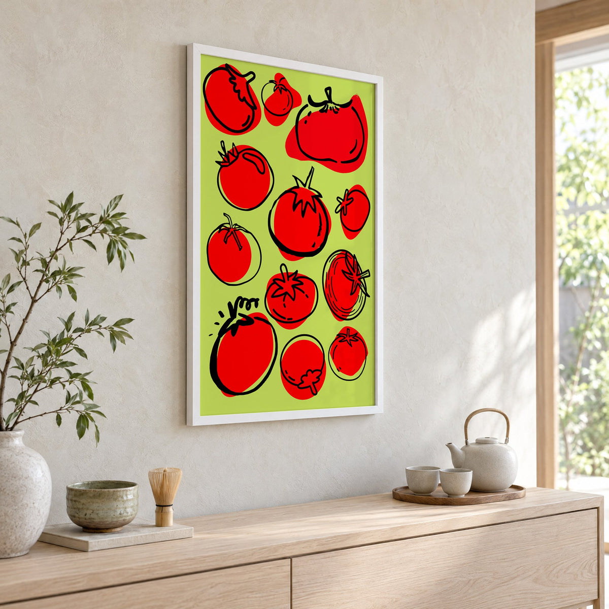 Red tomatoes on lime green print in a white frame above a pale wood console with a matcha tea set