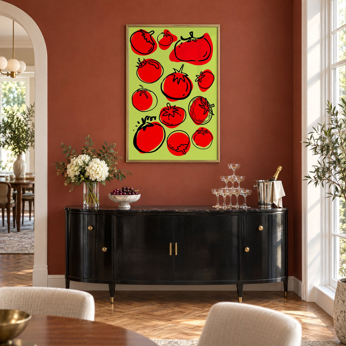 Red tomatoes on lime green print in a brass frame on a terracotta wall above a black buffet with a champagne tower