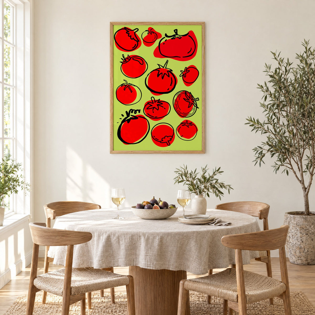 Red tomatoes on lime green print in an oak frame above a round linen-covered dining table with figs and wine