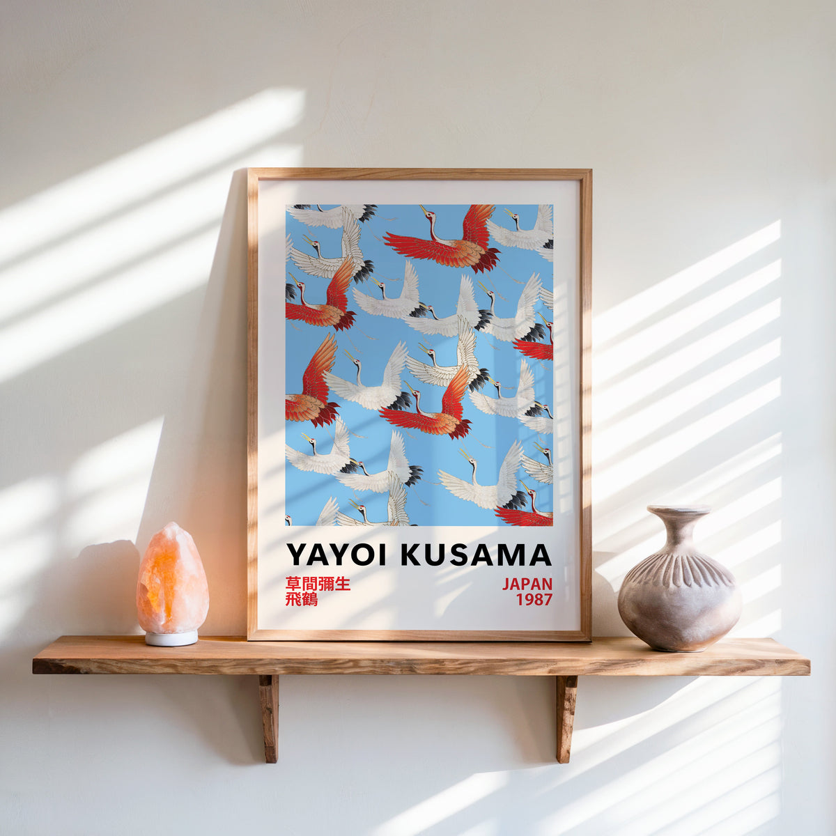 Yayoi Kusama inspired red and white flying cranes print in an oak frame on a live edge shelf beside a salt lamp