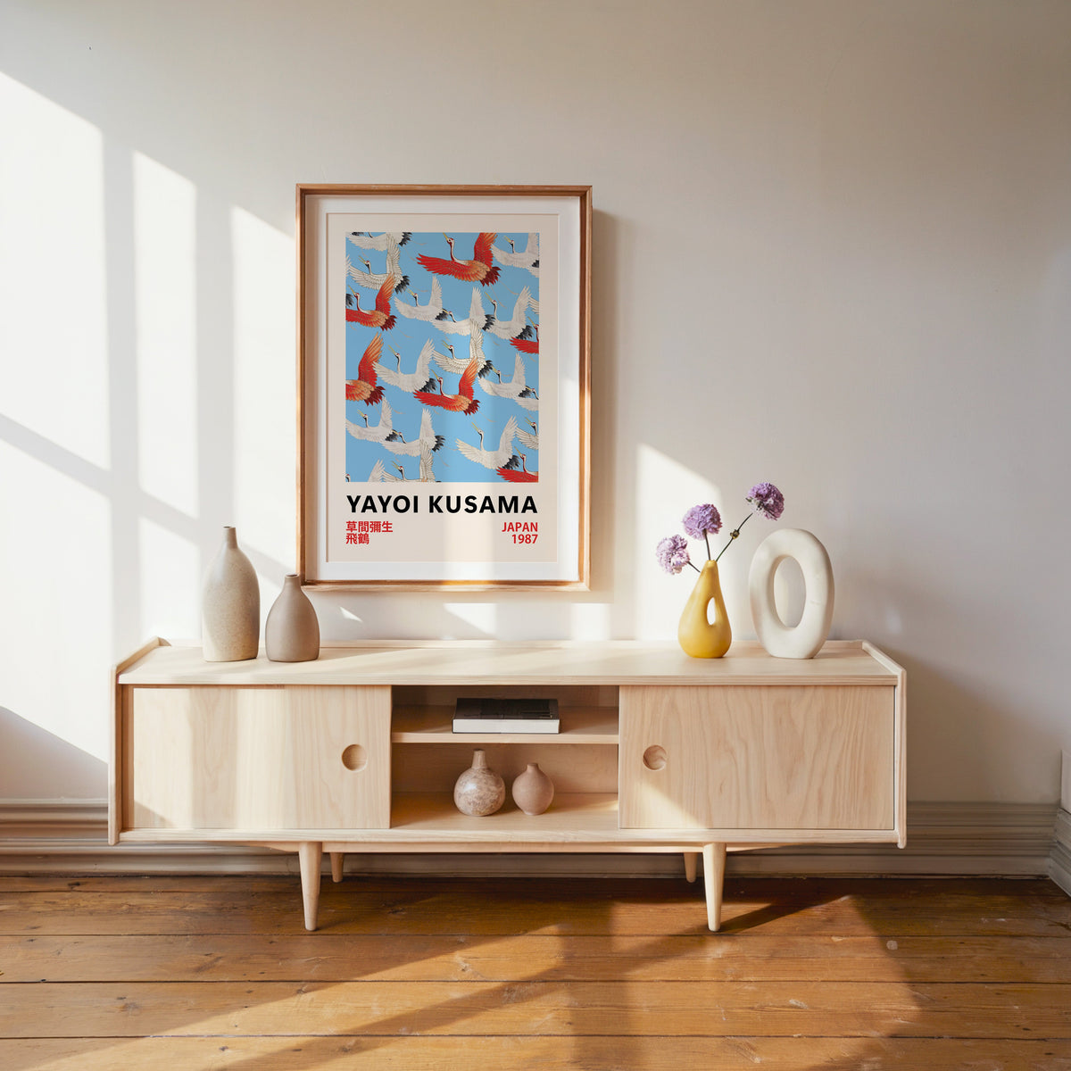 Yayoi Kusama inspired red and white flying cranes print in a wood frame with white mat over a pale media console