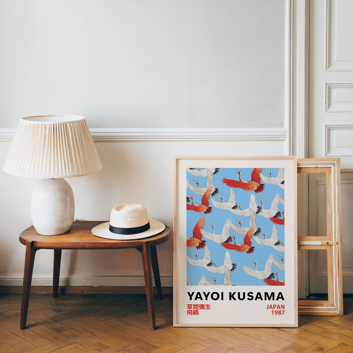 Yayoi Kusama inspired red and white flying cranes print in an oak frame over a bench with a panama hat