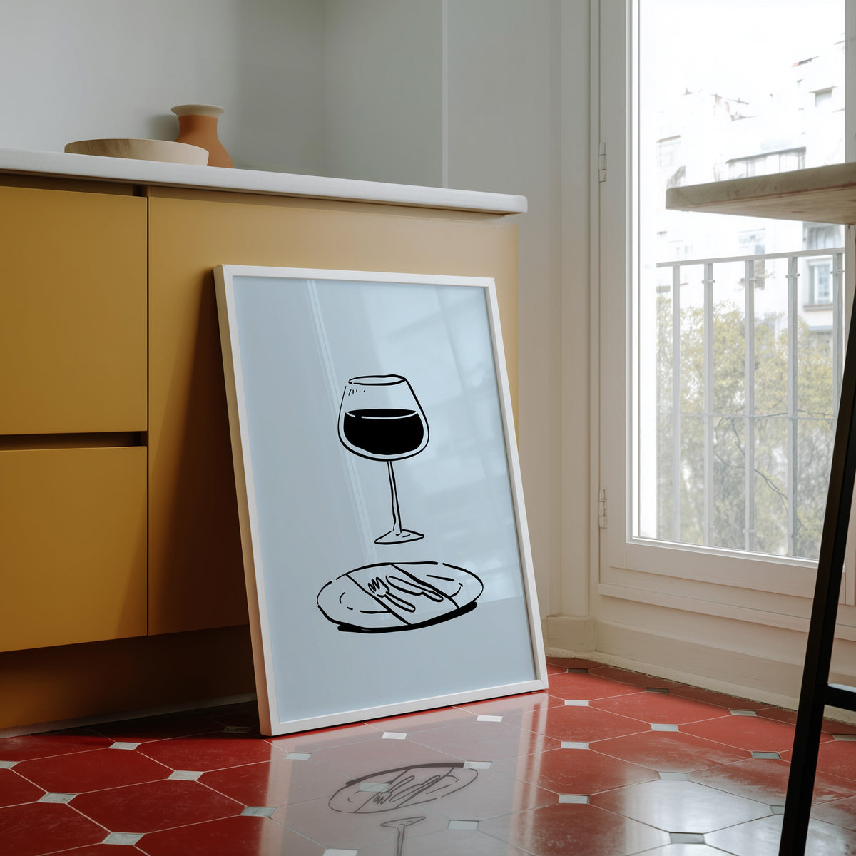 Red wine glass print in a white frame against yellow cabinets on a red tiled floor