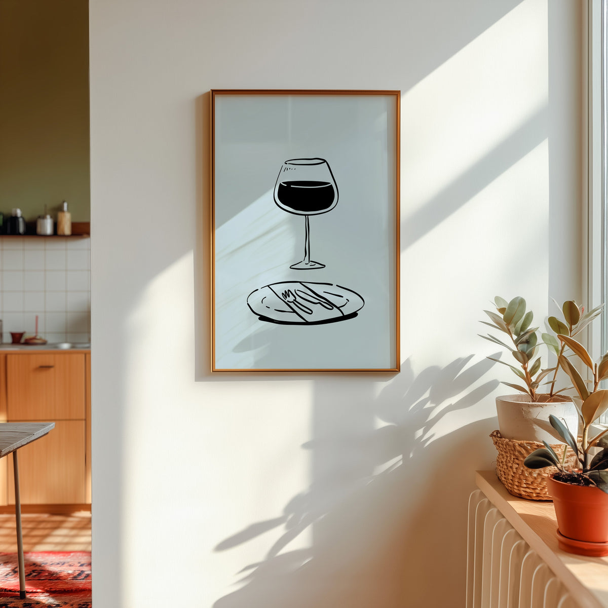 Red wine glass print in a gold frame in sunlight with plants and a kitchen beyond