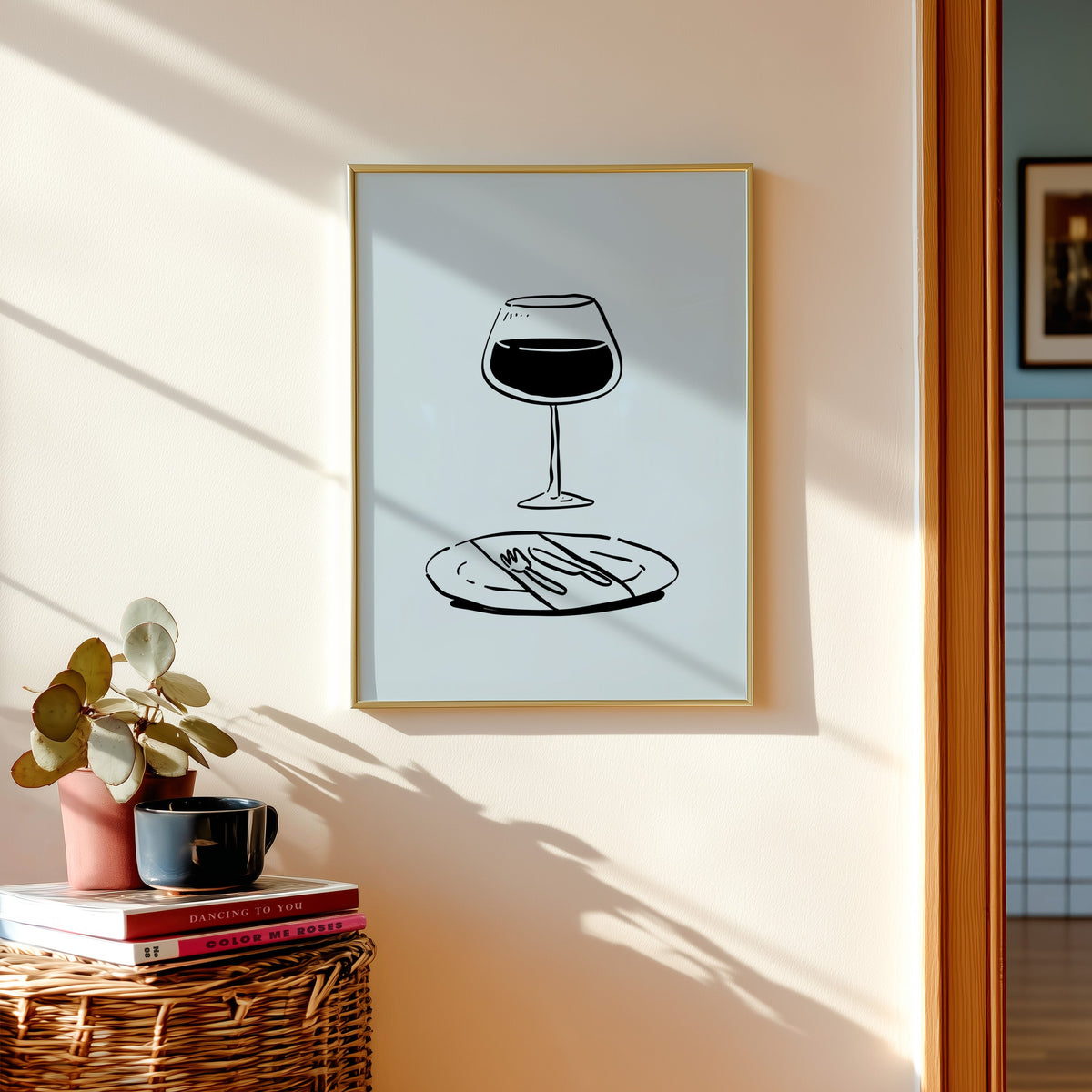 Red wine glass print in a gold frame above a basket of books and a pilea plant