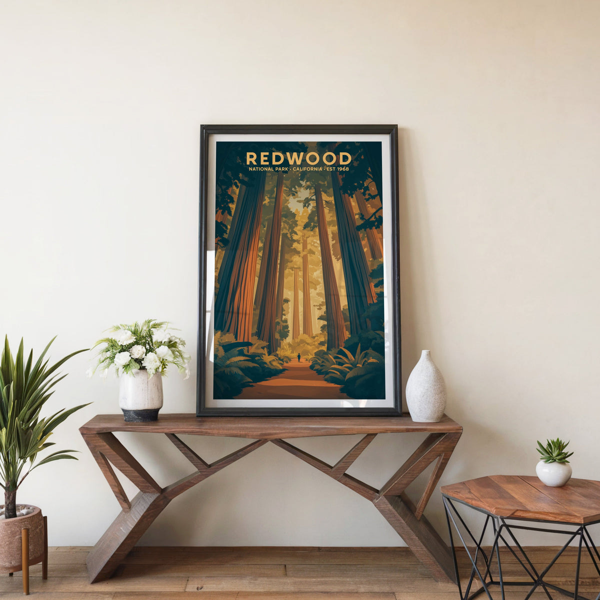 Redwood poster in a black frame on an entryway console table beside white flowers and a yucca