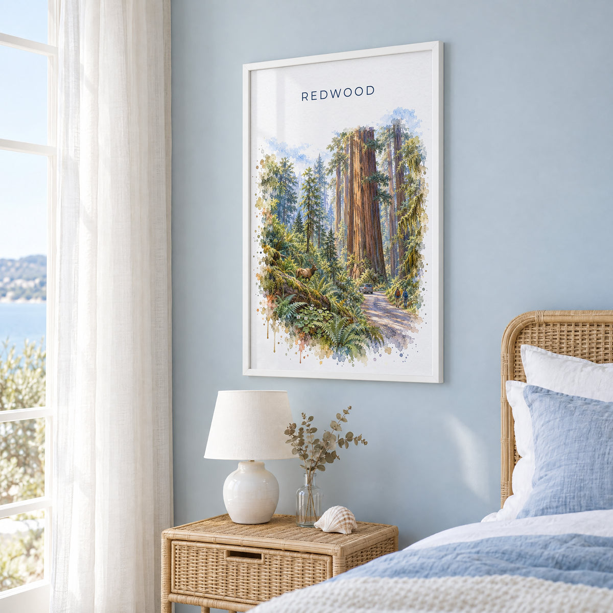 Redwood National Park watercolor print in a white frame on a pale blue wall beside a rattan bed in a coastal bedroom