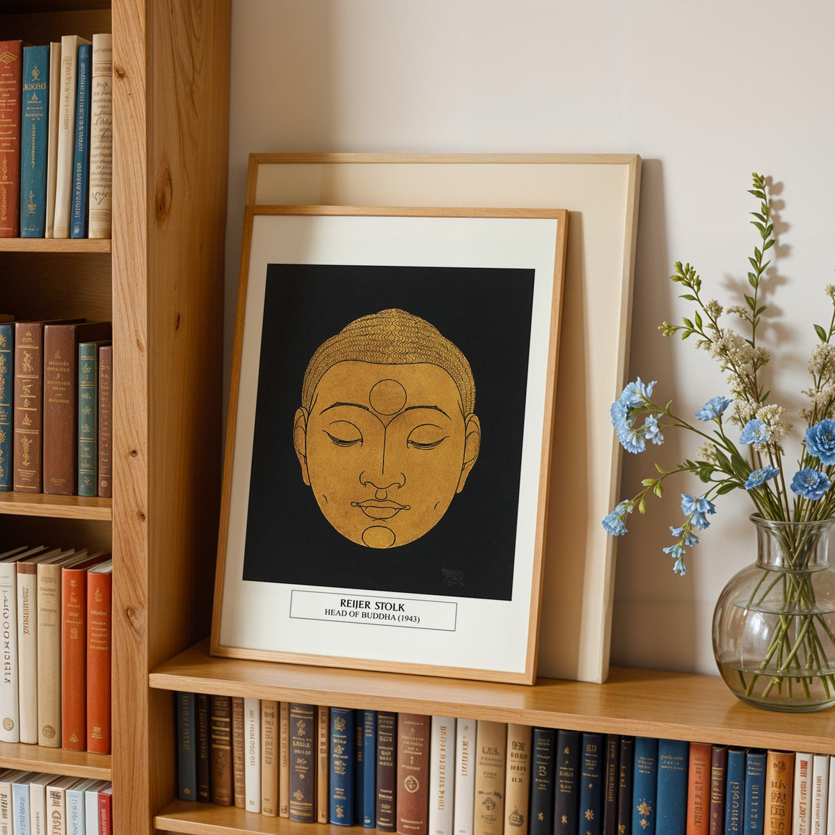 Gold and black print in an oak frame leaning on a bookshelf beside flowers