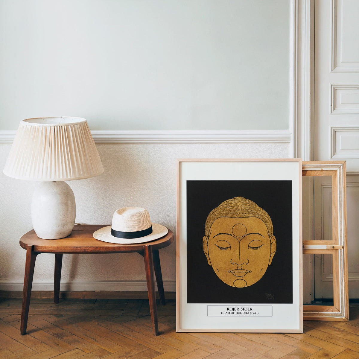 Buddha line art poster in a light wood frame leaning by a bench and hat
