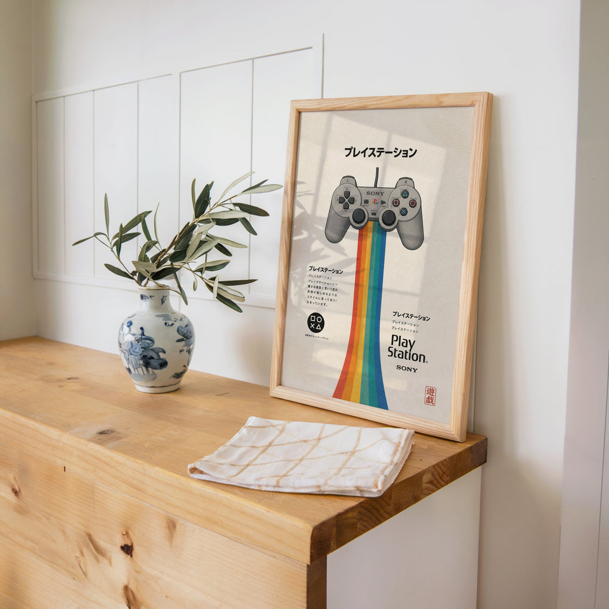 retro game controller with rainbow print in a pine frame on a wooden counter beside a blue and white porcelain vase