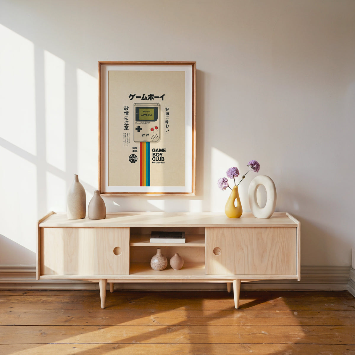 retro handheld game console with rainbow print shown in a wood frame with a white mat above a pale wood media console