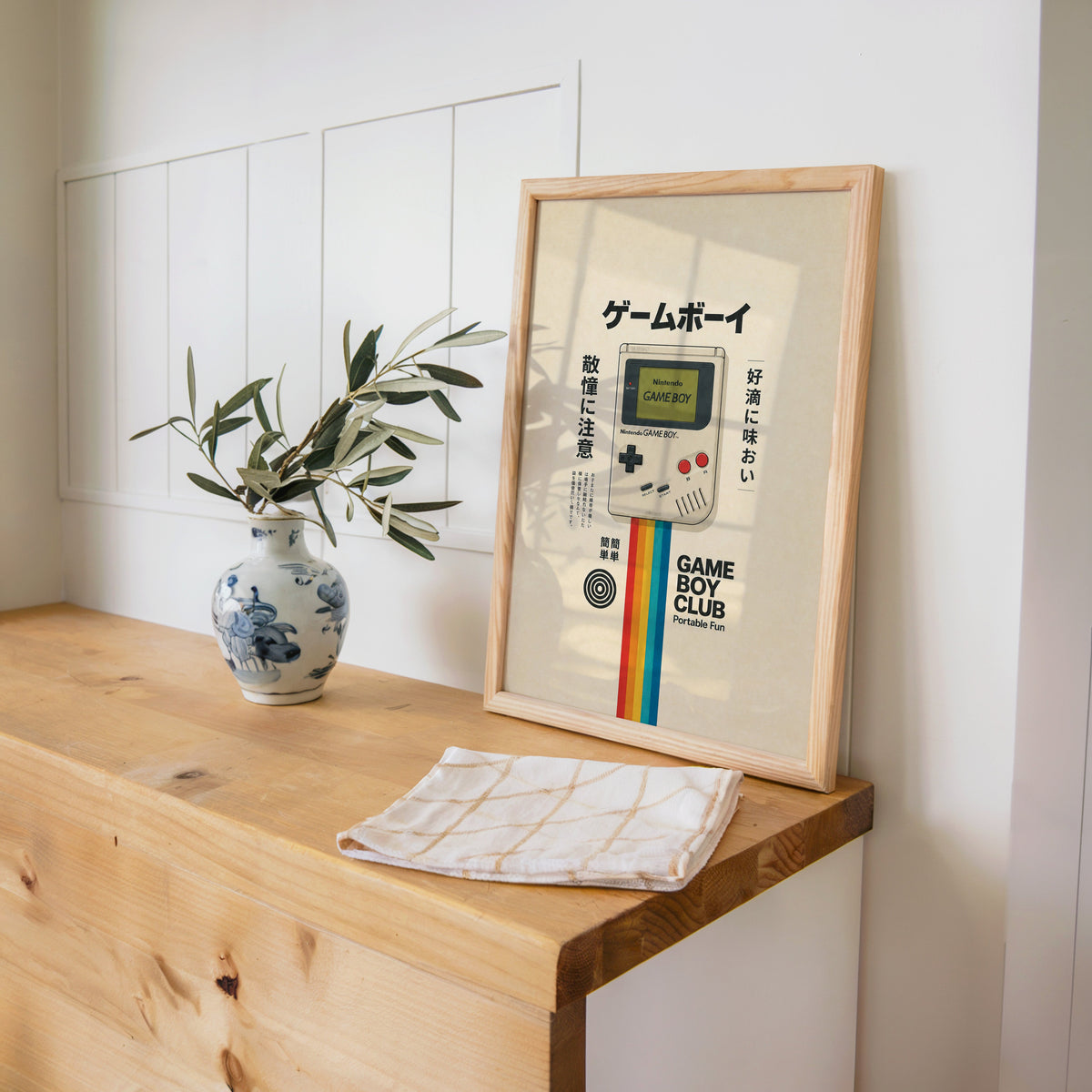 retro handheld game console with rainbow print in a pine frame on a wooden counter beside a blue and white porcelain vase