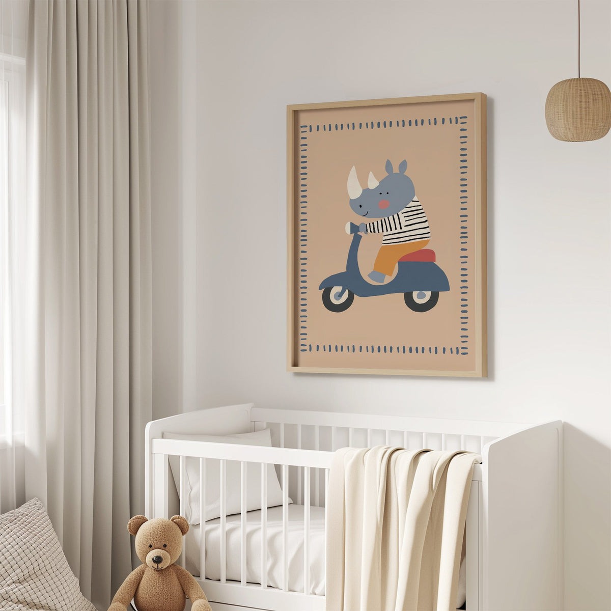 Rhino on a blue scooter nursery print in an oak frame above a white crib with a teddy bear